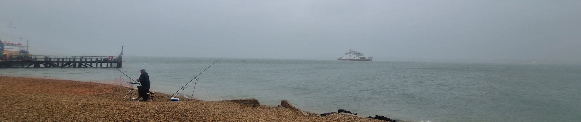 Fisherman on Calshot beach on a rainy day with the Red Funnel Ferry in the background