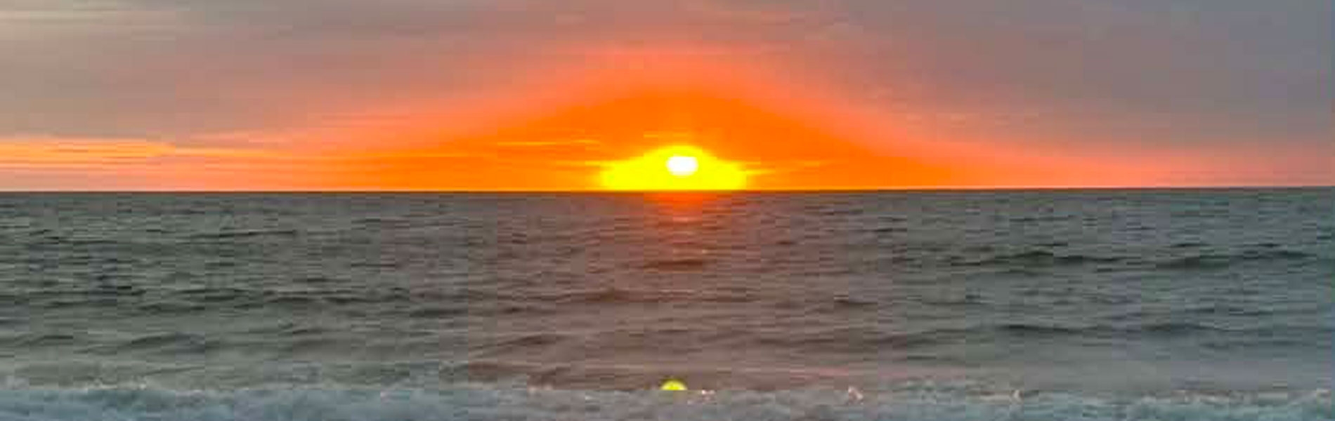 Sun setting on the horizon at Penbryn